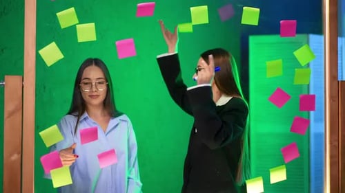 Caucasian women with long brunette hair wearing glasses stand at glass board.