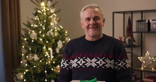 Happy Senior Man Holding Christmas Present Indoors