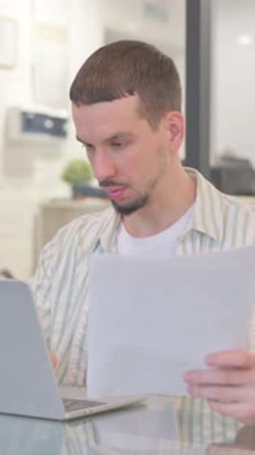 Young Man Works with Laptop and Documents Indoors