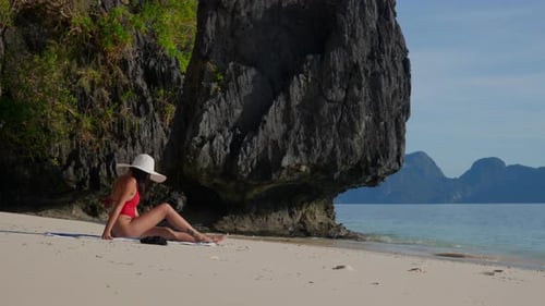 Mulher está sentada ao lado de uma enorme rocha na praia de Entalula