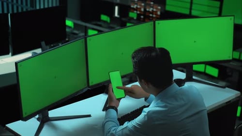 Man Using Mobile Phone Green Screen And Multiple Monitor With Mock Up Green Screen In office