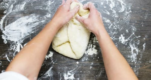 Hands Kneading Dough on Floured Wooden Surface