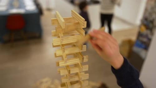 Child placing final wooden blocks on high tower during family playtime at home, teamwork,