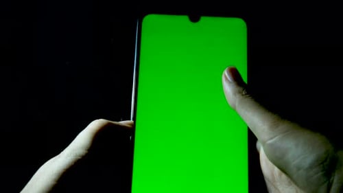 using smartphone with green screen on mobile phone. scrolling up. black background. close up. two ha
