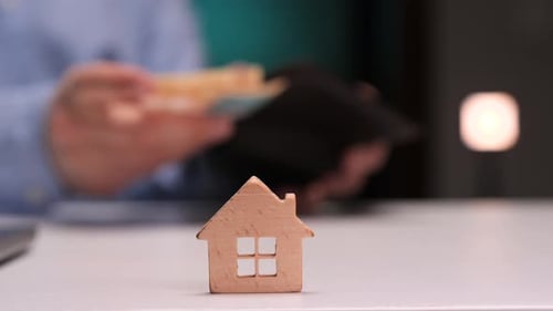 Wooden House and Counting Money on a Desk