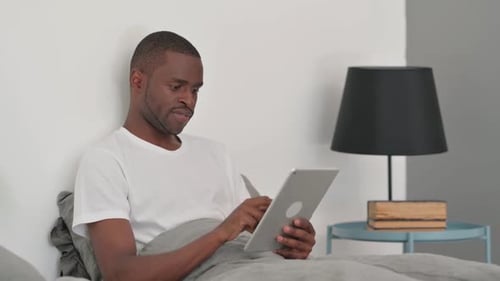 Man Using Tablet while Sitting up in Bed