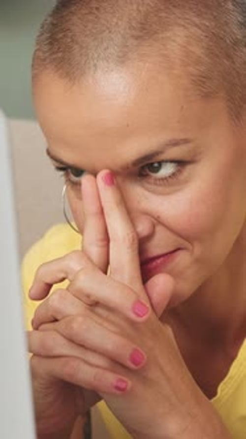 Close-up bald smiling woman using laptop while lying on sofa in living room