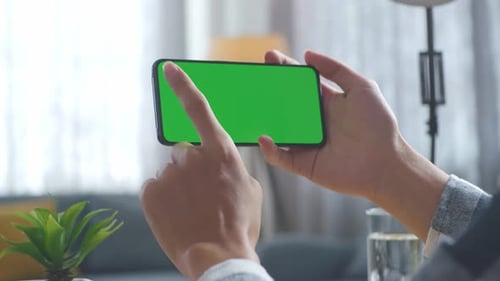 Close up of man's hands using a mock up green screen smartphone on a desk