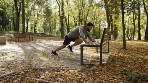 A Young Sportsman is Doing Physical Exercises Near a Park Bench