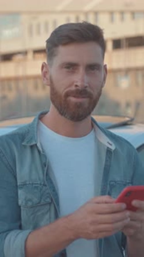 A Casually Dressed Man is Texting on His Smartphone While Enjoying the Outdoors in the City