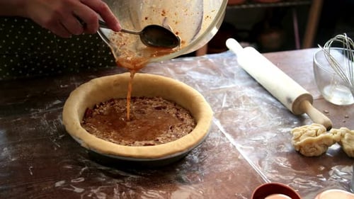 Woman Pouring Pecan Filling into a Pie Crust in a Home Kitchen