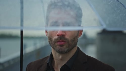 Mann steht unter einem Regenschirm an einem Regentag am Fluss in einem Stadtbild