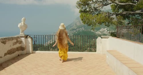 A woman enjoying walk in the garden. Female in yellow dress admires the sea view from a balcony with