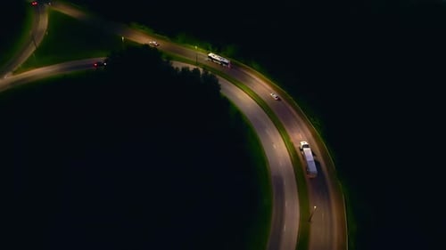 Watch Captivating Aerial Footage of Vehicles on a Winding Road Through a Dark Forest Under City