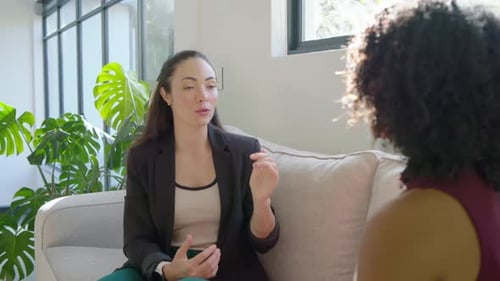 Diverses femmes sur un canapé, une femme de gauche commençant à parler en blazer, parlant, faisant des gestes, clarifiant