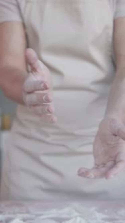 A baker claps his hands with flour as he prepares dough for baking homemade bread. Vertical shot.