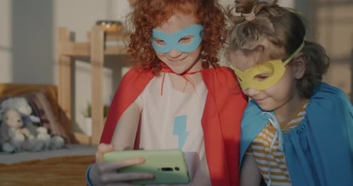 Children in Superhero Costumes Look at Cell Phone