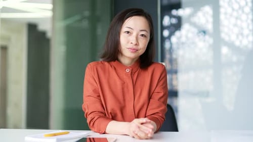 Webcam view. Asian woman watching video call training looking at camera while sitting at workplace