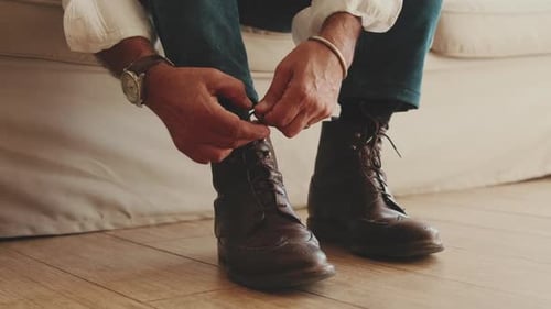 Close-up of legs of man putting on casual boots, tying shoelaces