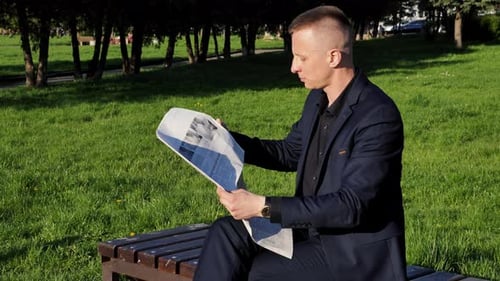 Young Student Reads Newspaper in Park Closeup