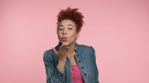 Young African American Woman Send Blow Air Kiss to you Posing on Camera Isolated on Pink Background