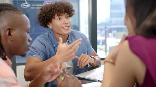 Discussing project, diverse team collaborating using laptop in modern office setting