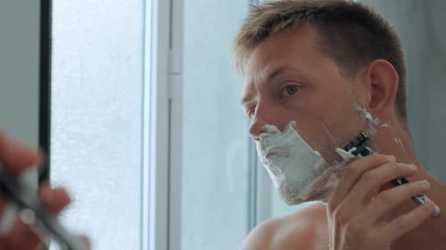 Caucasian Handsome Yong Man with Shaving Foam on His Face While Shaving His Beard Standing in the