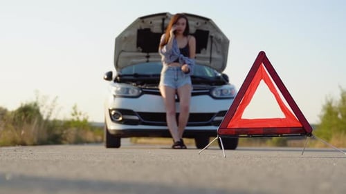 Road Side Warning Triangle Warning Oncoming Traffic of a Broken Down Car with a Woman Using Her Cell