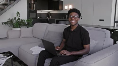 Young Man Using Laptop Smiling on Couch