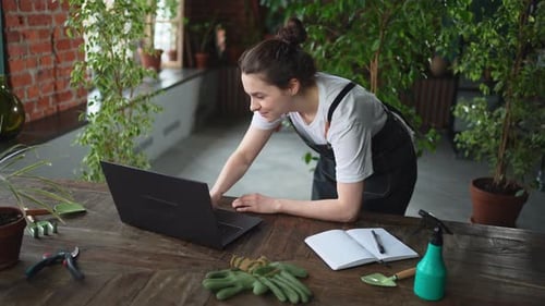 Female Florist Gardener Working in Botanical Store Greenhouse Using Laptop Order Plants