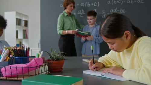 Teacher and Student Discussing Equations, Others Working at Desk in Class