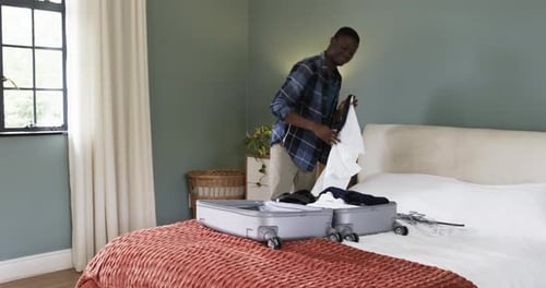 Man Packing Suitcase with Clothes in Bedroom