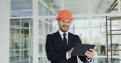 Smiling man CEO of building company looking at camera with digital computer while inspecting unfinis