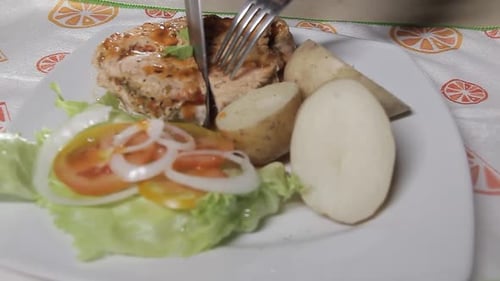 Close-up of chef cutting chicken with vegetables on white plate, healthy home cooking concept.