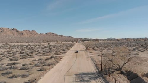 Slow motion drone shot of car going through desert in Palmdale, California on a bright clear day.