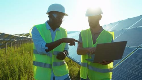 Slow Motion Two Men Use Laptop on the Solar Farm in Special Uniform Walking Discuss the Installation