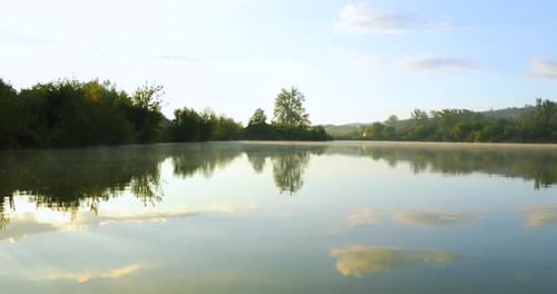 A view of the lake surface at sunrise when the mist rises above the water and the sun shines behind