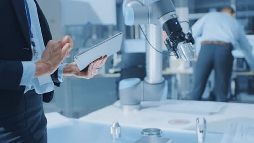 Engineer Using Tablet With Robot Arm in Factory