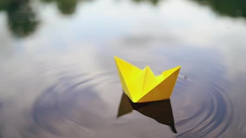 Woman's hand launches paper boat on the water. Paper boat sails along the river.
