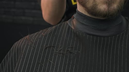 A Barber in a Barber's Shop Cuts the Hair of a Young Man with a Beard The Clipped Locks of Hair Fall