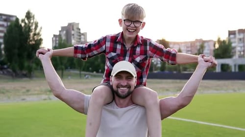 Happy child sits on father's shoulders. Family walk in nature. Father plays with child.