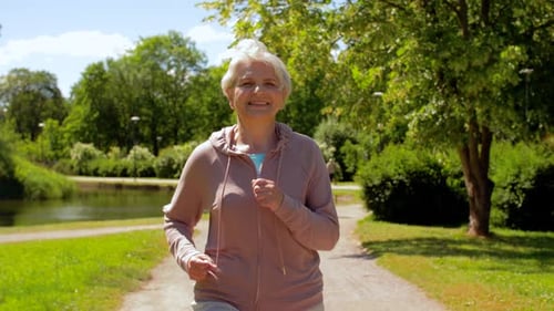 Smiling Senior Woman Jogging Through Sunny Green Park