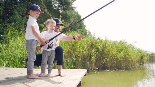 Vater mit zwei kleinen Kindern und Söhnen fängt Fische, die auf einer Holzbrücke oder einem Pier stehen. Familie Papa