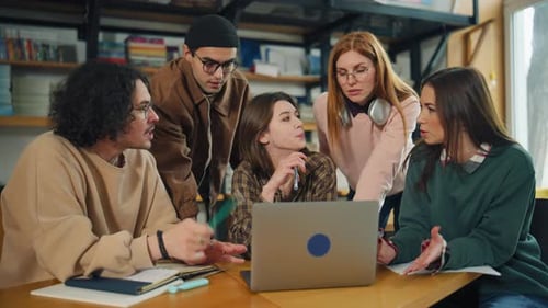 Gruppe von Studenten, die zusammen in einer Bibliothek lernen, dabei auf einen Laptop schauen und über ihre Arbeit diskutieren