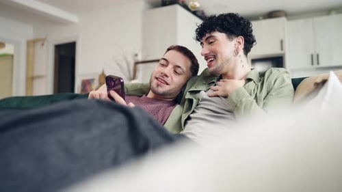 Affectionate Gay Couple Using Smartphone on the Sofa