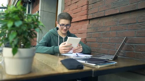 Young schoolboy studies and browses tablet in cheerful city cafe environment