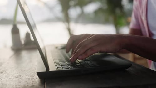 Man Types on Laptop at Sunset Beach Cafe Freelance Writer Works Remotely Near Sea Closeup on Hands