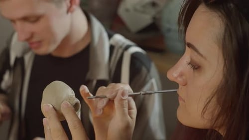 Woman Sculpts Clay Figure with Tool in Art Studio