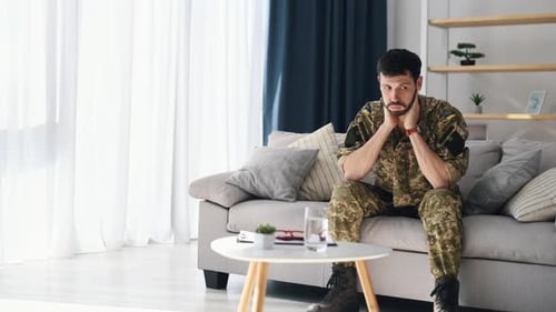 Man in Uniform Sits on Couch Indoors Contemplating