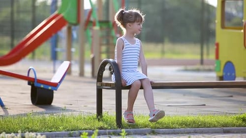 Cute Child Girl Waiting for Her Mother Sitting on a Bench on Summer Playground in Kindergarten Yard
